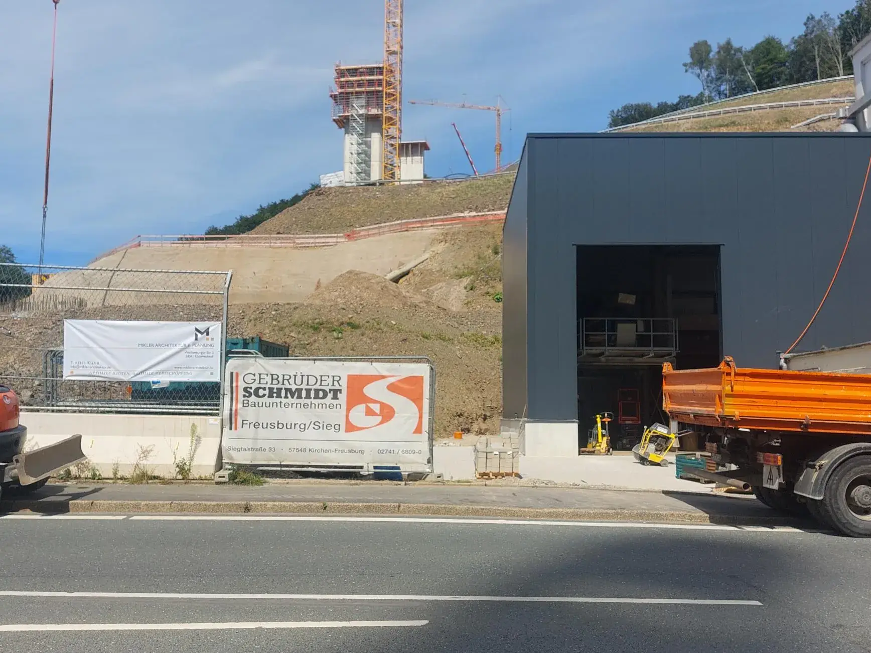 Betriebserweiterung Immel Seckelmann in Lüdenscheid: dunkler Neubau an der Straße, dahinter der Hang