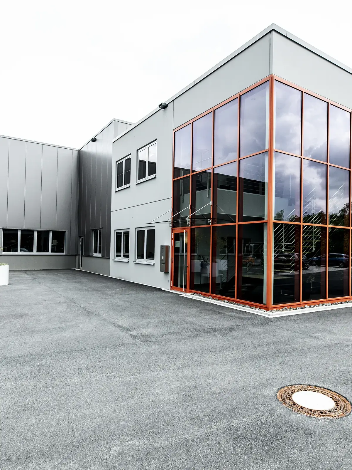Betriebsneubau Radolid in Schalksmühle: zweigeschossiger Kopfbau mit orange gerahmter Glasecke vor der Produktionshalle
