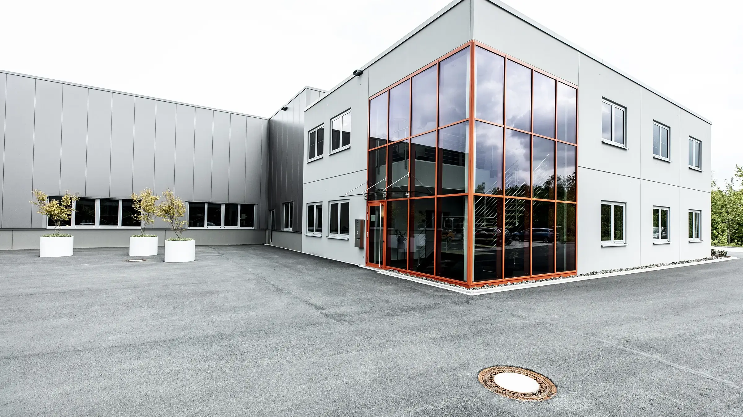 Betriebsneubau Radolid in Schalksmühle: zweigeschossiger Kopfbau mit orange gerahmter Glasecke vor der Produktionshalle
