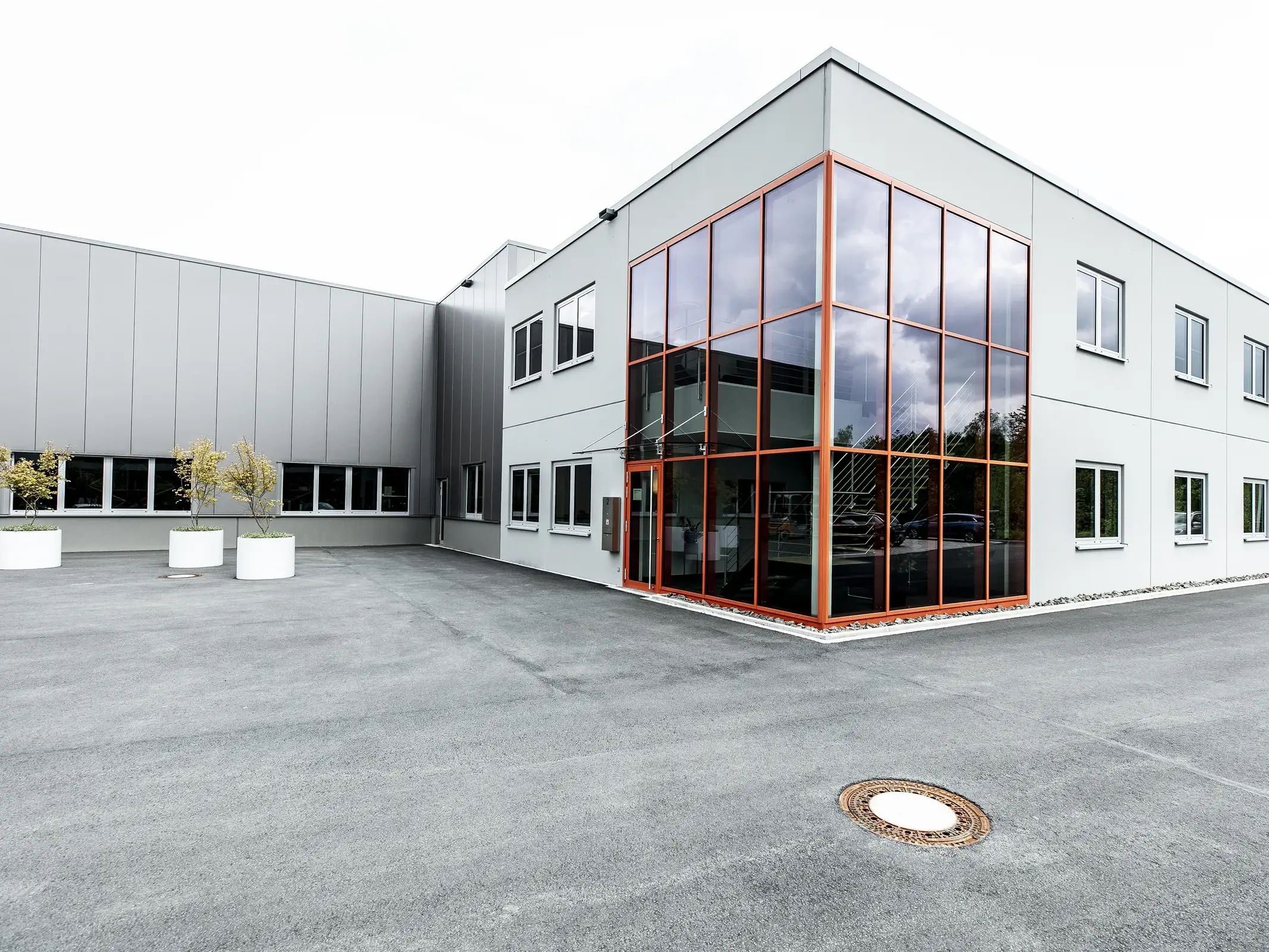 Betriebsneubau Radolid in Schalksmühle: zweigeschossiger Kopfbau mit orange gerahmter Glasecke vor der Produktionshalle